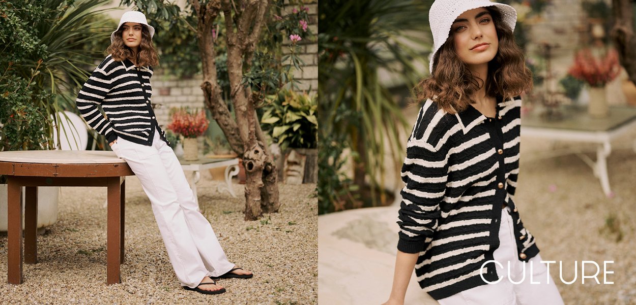 Black and cream striped cardigan with buttons, paired with white wide-leg pants and black sandals, set in a garden with plants.