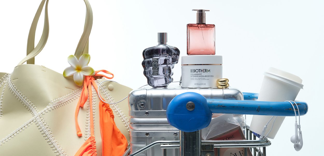 Beige tote bag with orange accent, floral detail; silver and purple perfume bottles; white cream jar; coffee cup; blue metal cart.