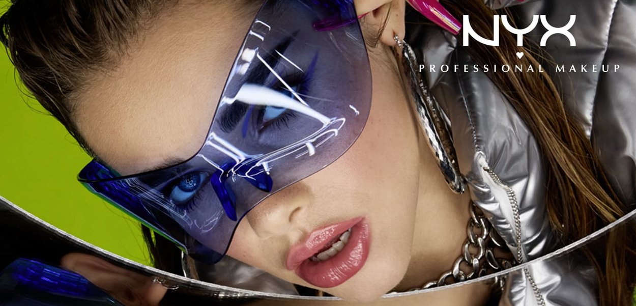 Futuristic blue-tinted sunglasses with oversized angular design. Model's glossy lips and silver metallic jacket reflect light. Bright green background.