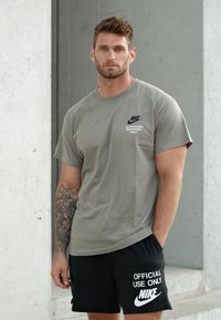 T-shirt cinza de algodão com um logótipo da Nike e texto. Combinado com calções pretos com texto e logótipo brancos. Modelo a exibir um estilo casual.