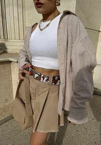 Prugasta bež oversized košulja s dugim rukavima, složena preko bijelog krojenog topa, u kombinaciji s bež suknjom, remenom s uzorkom kravljeg krzna i bež torbom na rame.