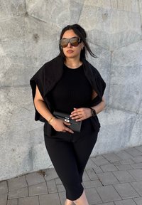 Crni top bez rukava s omčom i skraćenom dužinom, uparen s uskim crnim hlačama. Dodatak čini crna torbica i veliki sunčane naočale.