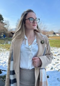 Casaco de lã bege com riscas azuis e brancas, camisa branca, saia cinza com textura, broche floral, fundo de relva nevada.