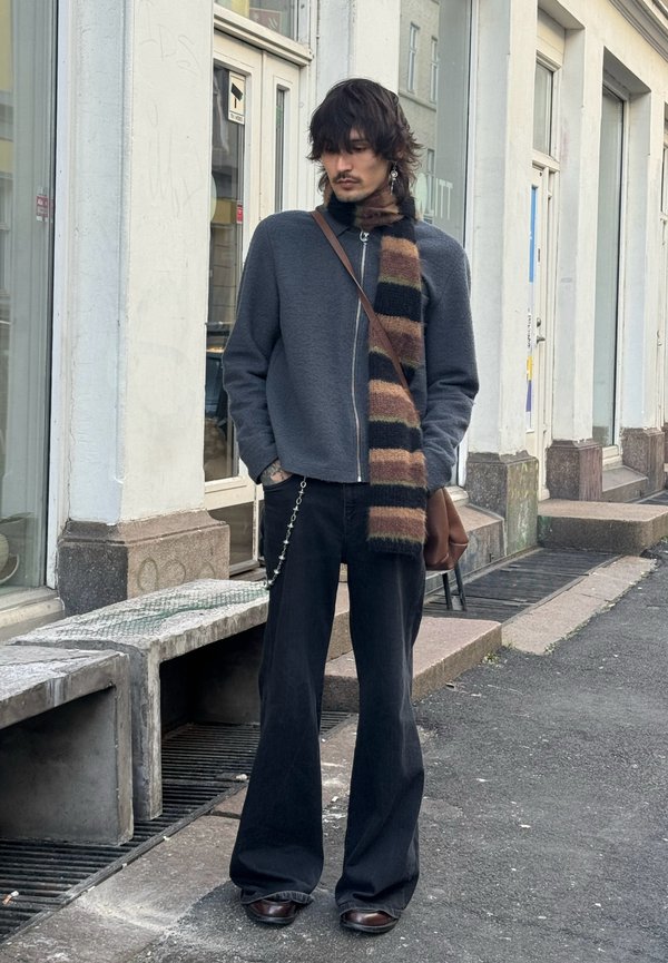 Grå fleecetrøje med lynlås, stribet strikket tørklæde i brunt og beige, sorte flared jeans, brune lædersko og crossbody-taske med kædedetalje.