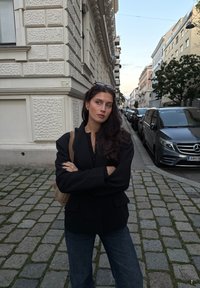 Czarna marynarka o luźnym kroju, z teksturowanej tkaniny, noszona na ciemnej bluzce. Niebieskie szerokie jeansy, brązowa torebka na ramię i okulary przeciwsłoneczne na głowie. Kocie ulice.