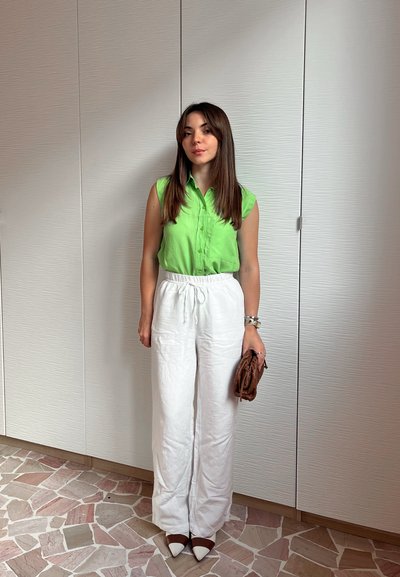 Camisa sin mangas verde, pantalones de lino blancos y sueltos con cordón, bolso de mano marrón y tacones de punta bicolor. Diseño simple y líneas limpias.