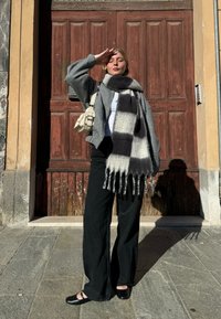 Pelēks vilnas maisījuma žakets, balts t-kreklis, melni platajiem kāju bikses un liels melnbalts kabatas lakats ar pušķiem. Melnas kurpes un maza bēša soma.