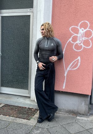 Tops de manga larga, ajustado, de color gris oscuro con un cuello con cremallera, combinado con pantalones negros de pierna ancha. Los accesorios incluyen múltiples anillos y pulseras.