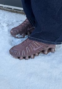 Baskets Nike violettes avec semelles incurvées uniques portées avec un jean bleu foncé, debout sur la neige.