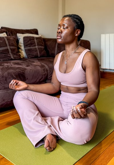 Mujer con un sujetador deportivo de color rosa claro yleggings de canalé a juego, sentada con las piernas cruzadas sobre una esterilla de yoga verde, con los ojos cerrados, meditando.