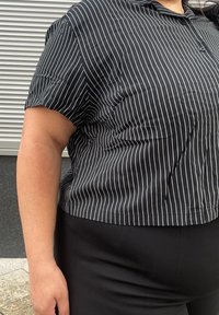 Sort og hvid stribet kortærmet blouse, let vævning, knap-åben krave, med en afslappet pasform og let glans. Kombinationen med sorte tætsiddende bukser.