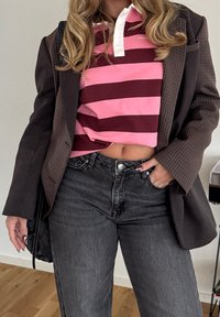 Blazer marron texturé porté sur un polo rayé rose et bordeaux, associé à un jean noir taille haute. Détail notable : un col blanc.