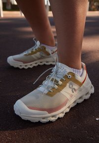 Leichte Laufschuhe in Weiß, Gelb und Pink mit atmungsaktivem Obermaterial, gepolstertem Schuhkragen und strukturiertem Sohlenprofil. Mit kontrastierendem Logo und Schnürsenkeln.