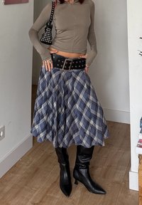 Maglia marrone chiaro a maniche lunghe; gonna a quadri blu; cintura nera con borchie; stivali neri alti al ginocchio con punta; piccola borsa nera con borchie.