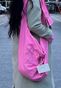 Rosa tygkasse med en stor huvudfack, sidoficka och en avtagbar ID-hållare. Materialet verkar mjukt och något glansigt.