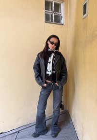 Mustast nahast jakk tumeda pluusi kohal, millele on kombineeritud laienevad tumedad teksad. Kaunistatud must-valge mustriga salliga ja päikeseprillidega.