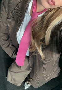 Hnedé sako s kockovaným vzorom a bielou košeľou, doplnené o v�ýraznú ružovú kravatu. Hnedé nohavice a strieborné metalické špicaté topánky dotvárajú vzhľad.