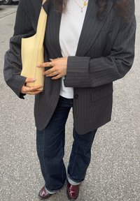 Blazer rayé gris porté sur un t-shirt blanc, jean évasé bleu foncé, tenant un sac en cuir jaune, accessoirisé avec plusieurs bagues.