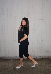 Fekete atlétatrikó és testhez simuló fekete leggings, fehér nyitott orrú magassarkúval párosítva, sötét fejkendővel kiegészítve. Varrás nélküli anyag és tiszta vonalak.