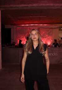 Svart ärmlös topp med skräddarsydd design, kompletterad med högmidjade byxor. Otydlig bakgrund med rosa belysning och en baravdelning.