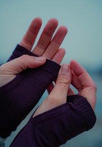 Mains ajustant les poignets d'un haut à manches longues de couleur violet foncé sur un fond flou en plein air.