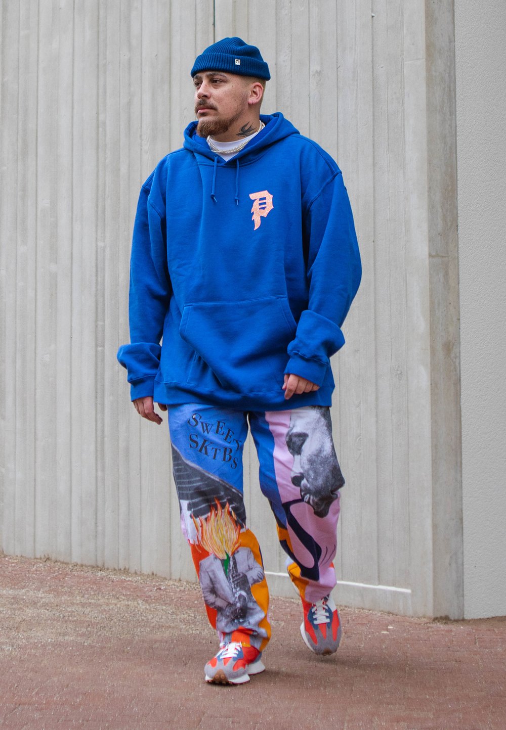 Fleece azul com um logotipo pêssego, calças de moletom estampadas com gráficos ousados e ténis coloridos. Ao estilo de um gorro azul.