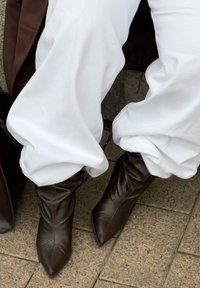 Bruine leren enkellaarsjes met een puntige neus en een gestructureerd patroon, gecombineerd met loszittende witte broek, rustend op een stenen oppervlak.