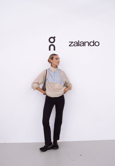 Suéter ligero en tonos beige y gris con un cuello alto, combinado con pantalones negros y calzado negro. Diseño sencillo, textura suave y corte relajado.