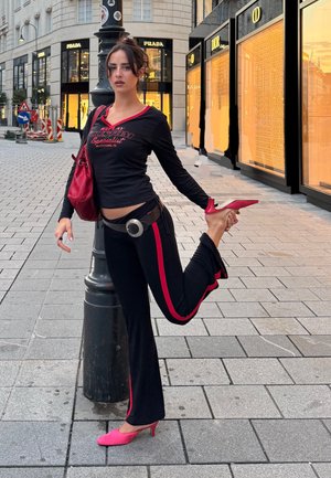 Top negro de manga larga con ribete rojo y texto gráfico, combinado con pantalones negros con rayas rojas y un cinturón plateado, acentuado por tacones rosas.