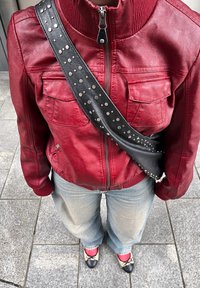 Giacca in pelle rossa con zip frontale, due tasche sul petto, abbinata a jeans a gamba larga di colore azzurro chiaro e ballerine nere con dettagli beige.