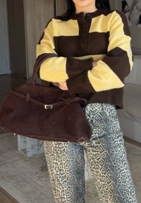 Pulôver de malha listrado em castanho e amarelo com fecho de botão, combinado com umas calças cinza com padrão de leopardo e uma bolsa de camurça castanha escura.