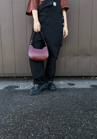 Μαύρες φόρμες με τσέπη, φανέλα σε χρώμα σκουριάς, καμπυλωτή μπορντό τσάντα και χοντρά μαύρα πα πούτσια με πλατφόρμα σε μια υφιστάμενη επιφάνεια.