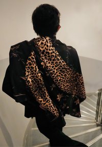 Écharpe noire à motif léopard avec des accents floraux, présentant une texture lisse, drapée de manière décontractée sur une tenue sombre.