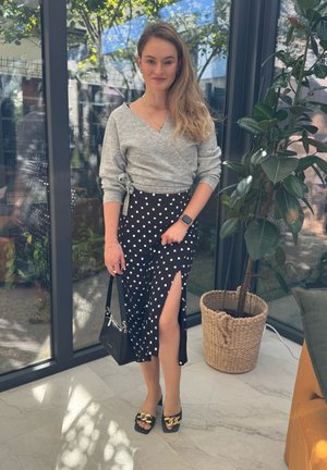 Suéter gris con envoltura, falda negra con lunares y abertura lateral, bolso negro y zapatos de plataforma negros con acento de cadena dorada.