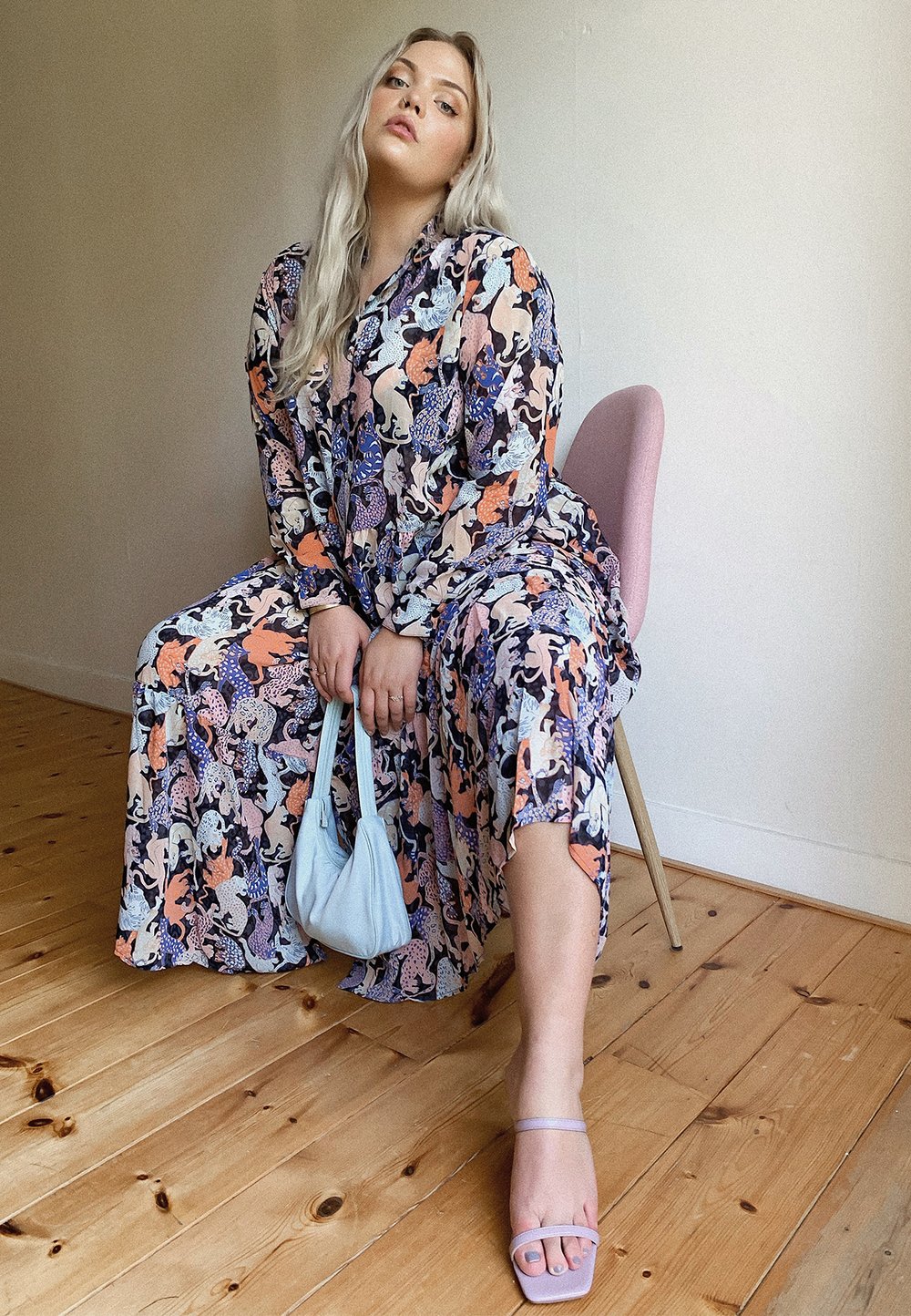 Floral maxi dress featuring a blend of blues, oranges, and pinks. Complemented by a light blue handbag and lavender sandals. Set against a wooden floor background.
