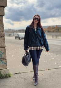 Sort oversizejakke, ternet skjorte under, marineblå leggings, knæhøje mørkebrune støvler og en sort håndtaske. Udendørs bymiljø.