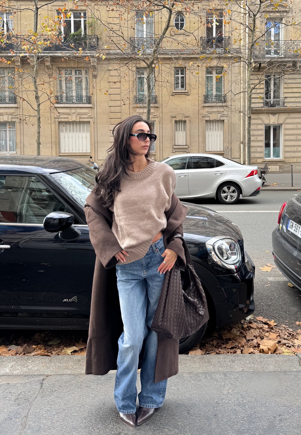 Beež kudumiga kampsun ümarate kaelustega, kombineeritud helesiniste lõhkuvate teksadega. Pruun mantel ja tekstuuriga tume käekott. Mustad päikeseprillid täiendavad välimust.