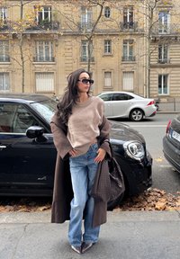 Beež kudumiga kampsun ümarate kaelustega, kombineeritud helesiniste lõhkuvate teksadega. Pruun mantel ja tekstuuriga tume käekott. Mustad päikeseprillid täiendavad välimust.