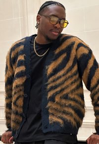 Cardigan en matière duveteuse, semblable à de la laine, présentant une base marine avec des rayures à motif animalier orange. Il est doté d'une fermeture à boutons et de manches longues.