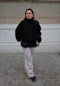 Veste bomber noire à col haut, superposée à un haut foncé à bordure en dentelle, associée à un pantalon évasé beige clair et des bottines noires.