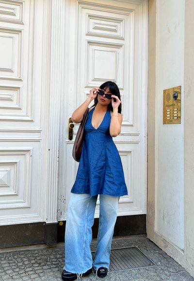 Top halter de denim en azul profundo, combinado con jeans de pierna ancha en azul claro. Los accesorios incluyen gafas de sol negras pequeñas y un bolso de hombro marrón.