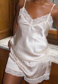 Set da pigiama in satin color crema chiaro, con delicati dettagli in pizzo sul colletto e sull'orlo dei pantaloni corti, dotato di spalline regolabili.