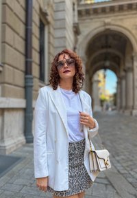 Vit dubbelknäppt kavaj över en vit T-shirt, tillsammans med en minikjol i leopardmönster. Accessoarer inkluderar en ljus handväska och solglasögon.