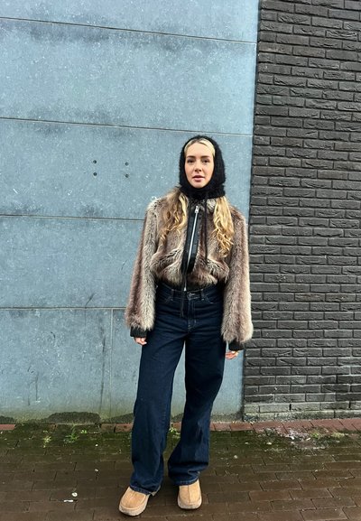 Chaqueta corta de piel sintética en gris con acentos negros, cuello alto, combinada con pantalones vaqueros de pierna ancha en azul oscuro y botas al tobillo en marrón claro.