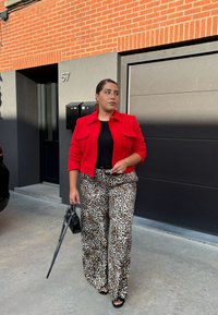 Rød tekstureret jakke over en sort top, parret med brede leopardmønstrede bukser. Accessoriseret med en lille sort taske og mørke solbriller.