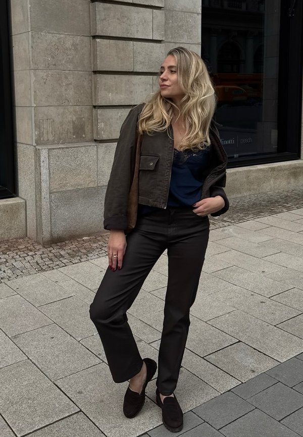 Olivgrüne, kurz geschnittene Jacke, marineblaue Spitzen-Cami, elegante schwarze Hose und dunkle Slipper; strukturierter Stoff mit lockerer Passform und subtilen Details.