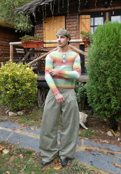 Suéter tejido multicolor de manga larga, combinado con pantalones cargo de gran tamaño en color verde oliva. Accesorios incluyen gafas de sol y una gorra.