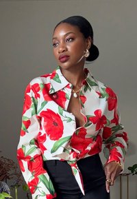 Camisa com estampa floral apresentando papoulas vermelhas e folhas verdes sobre um fundo branco, com um botão frontal e design de gola clássica.