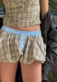Καφέ και μπεζ καρό σορτς με ελαστική μέση σε μπλε ρίγες και κουμπιά. Έχει κροσσάτη άκρη και  gathered υφή.