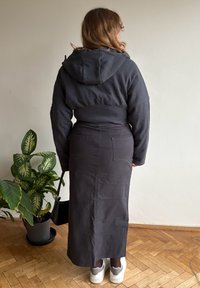 Tumehall kapuutsiga dress, millel on istuv talje ja lehvikukujuline seelik. Pehme kangas, kaks tagataskut, valgete tossudega, siseruumides.